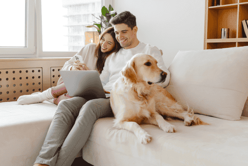Happy couple sitting on couch with their dog, enjoying home insurance peace of mind