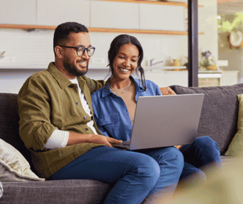 Happy couple sitting on couch using laptop to explore insurance options
