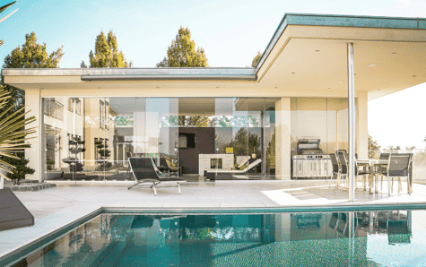 Poolside view of a modern villa with outdoor seating and clear blue water