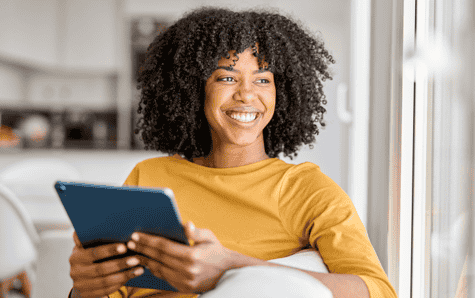 Smiling girl sitting on couch using tablet to browse insurance options