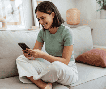 Smiling girl using phone while sitting comfortably on couch